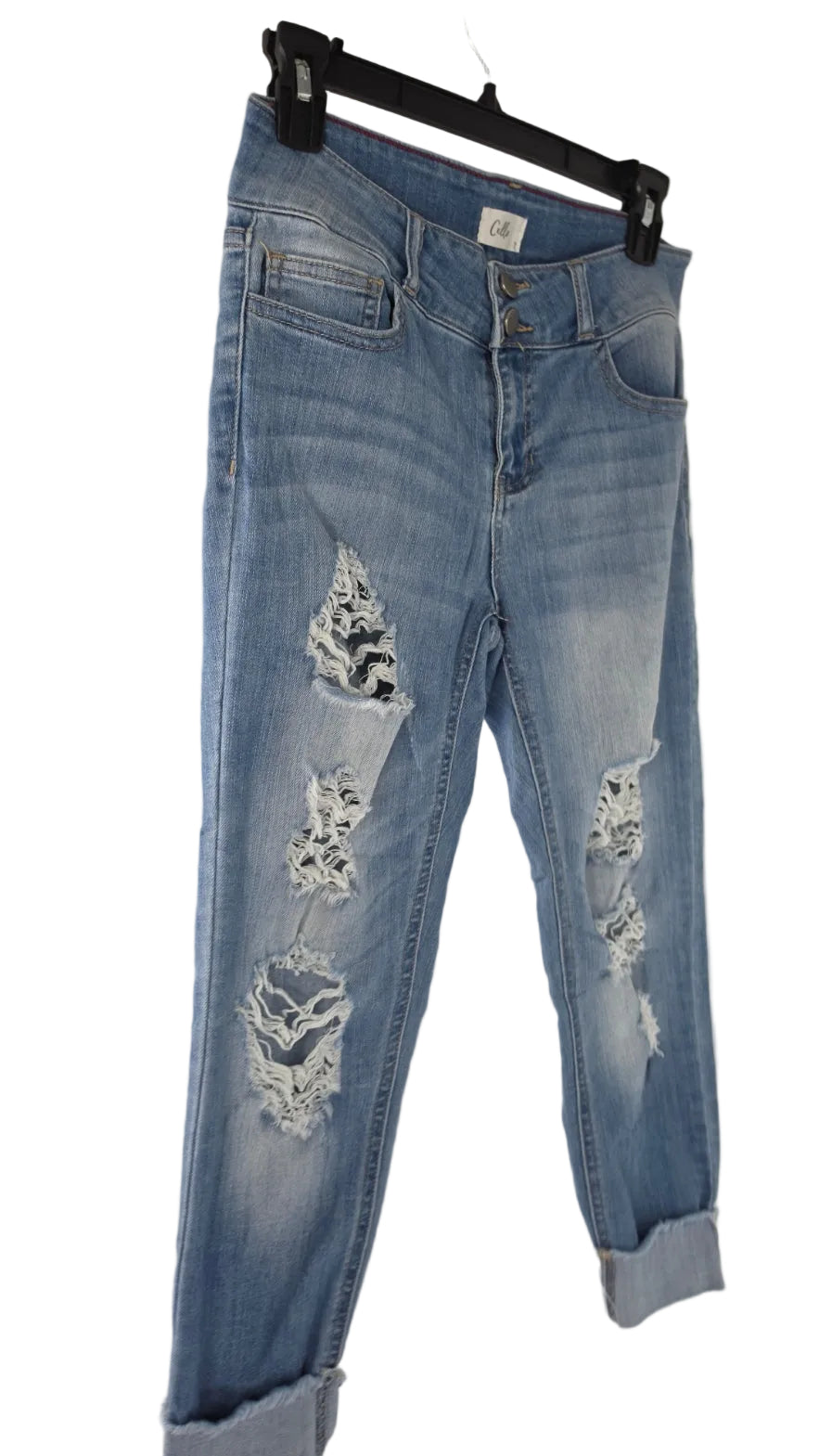 Light wash blue distressed denim jeans with ripped details and rolled cuffs, hanging on a black hanger against a plain white wall.
