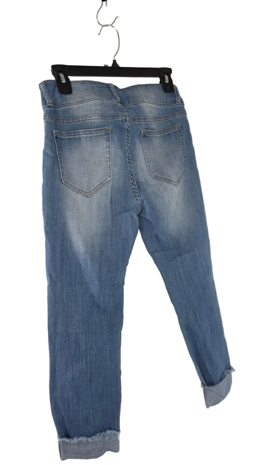 Light blue denim jeans shown from the back, hanging on a black hanger against a plain white wall corner.
