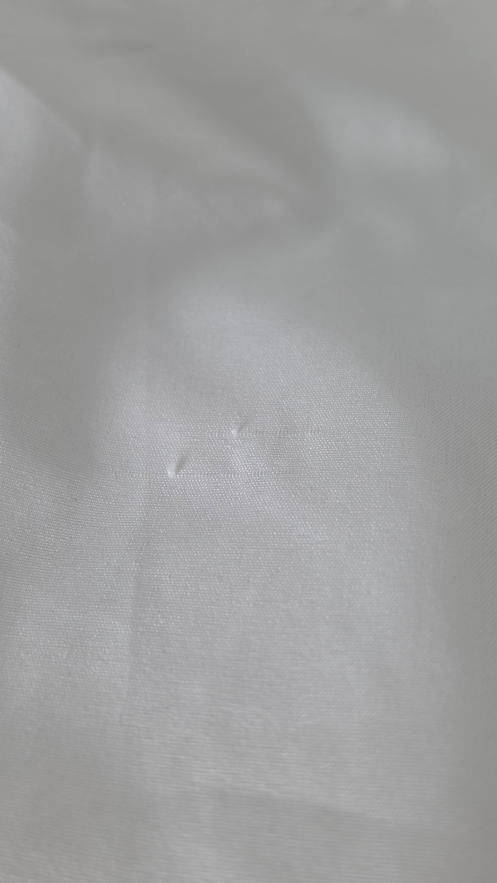 A close-up of white textured fabric with soft folds and a subtle woven surface.