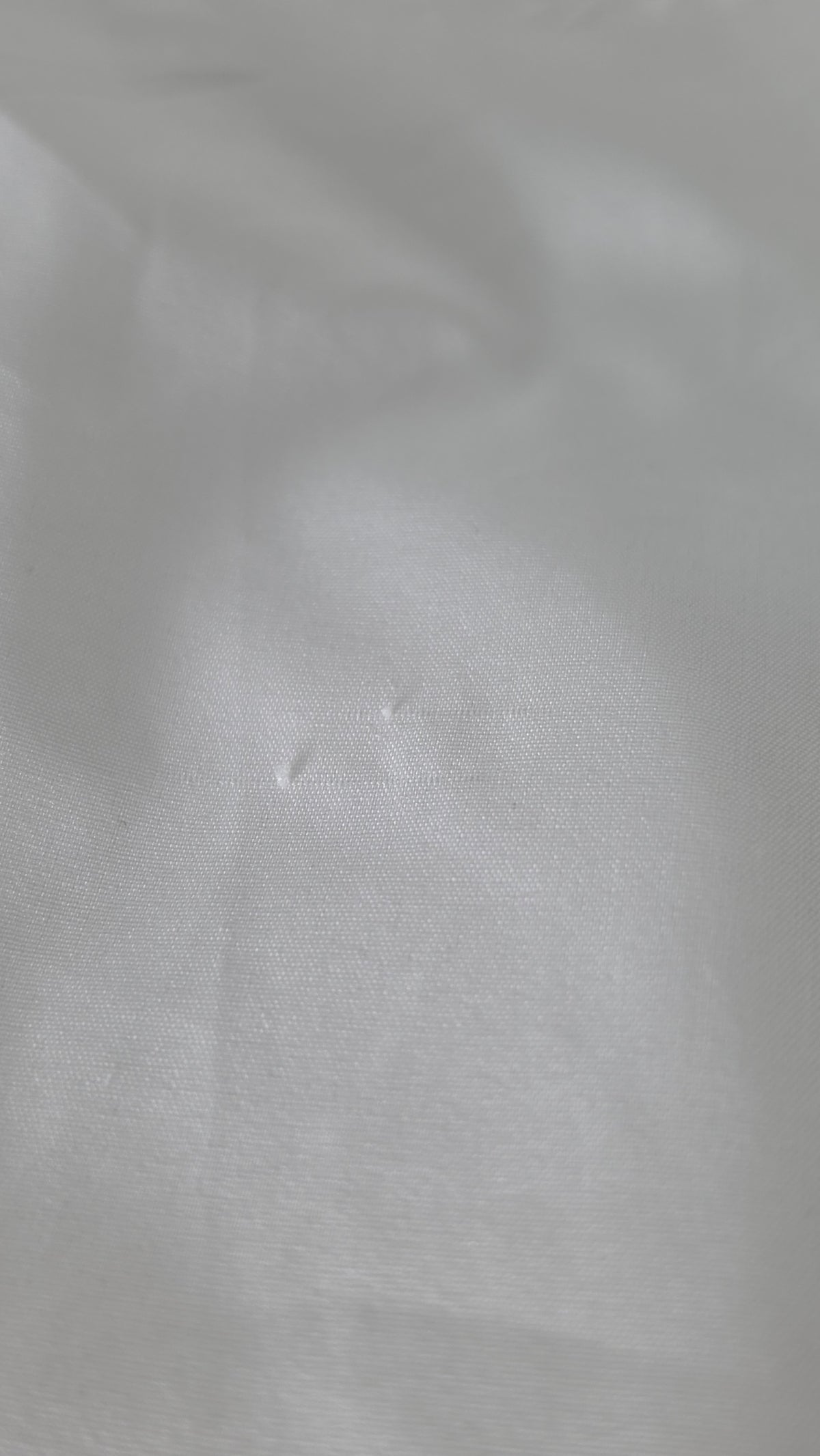 A close-up of white textured fabric with soft folds and a subtle woven surface.