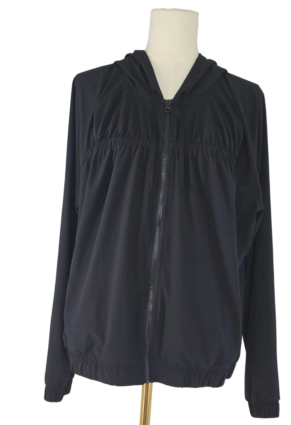 A black hooded zip-up jacket displayed on a white mannequin torso with a gold stand against a plain white background.