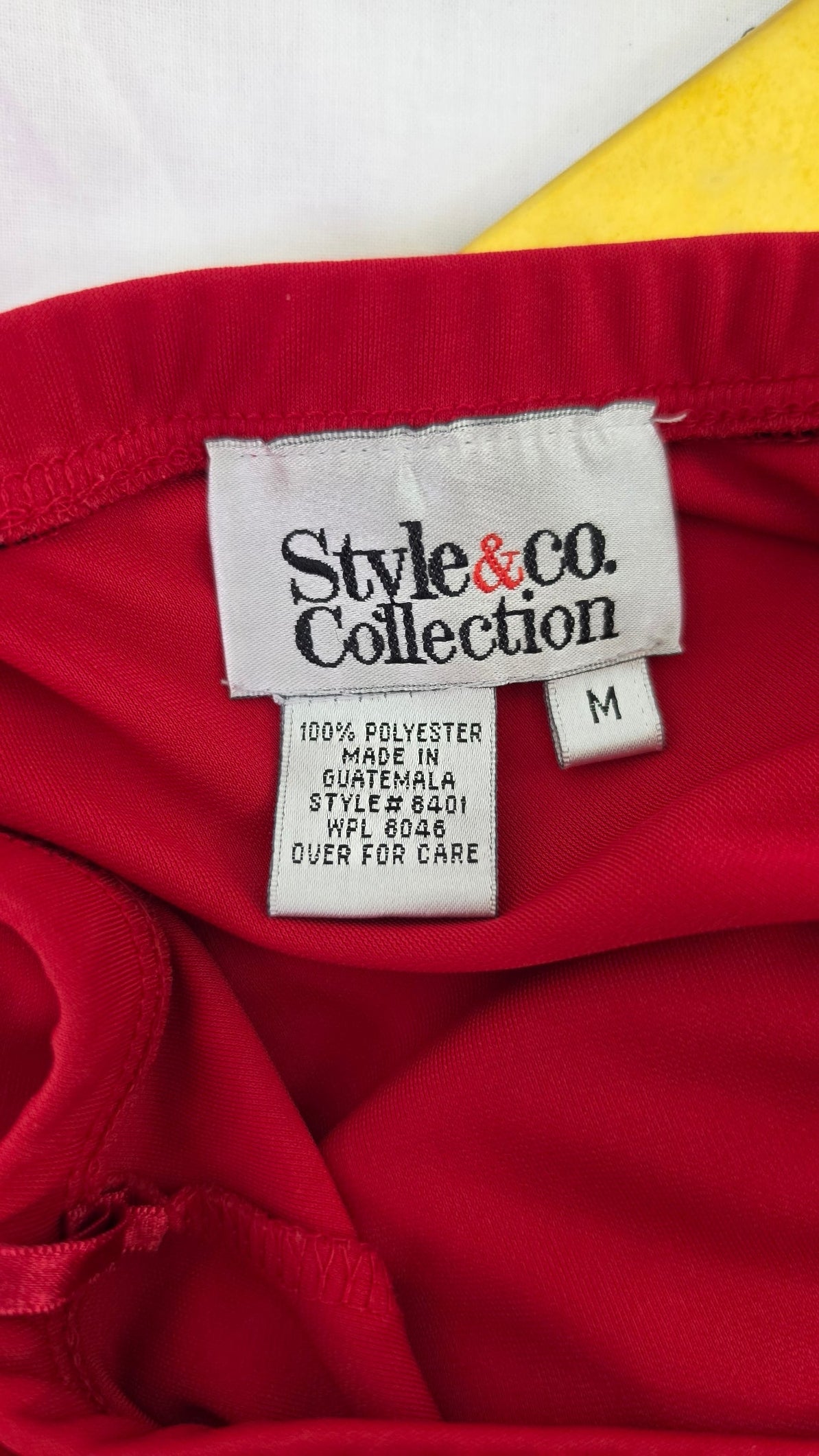 Close-up of a red garment's interior neck label area, showing a white Size M tag and a larger white brand tag reading Style & co. Collection.